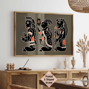May include: A framed print of three stylized figures in black and white with orange accents. The figures are standing in a row and appear to be wearing traditional clothing. The background is a muted green color.