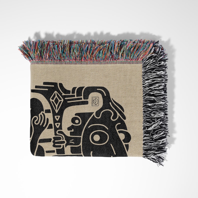 Pu&ograve; includere: Una coperta tessuta con un design grafico in bianco e nero di un viso stilizzato. La coperta ha un bordo a frangia con fili multicolori.