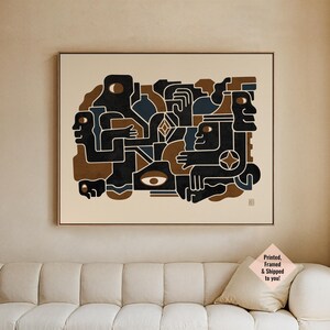 May include: Abstract art print with a geometric design of human-like figures in black, brown, and blue on a cream background. The artwork is framed in a dark frame and hangs above a cream sofa.
