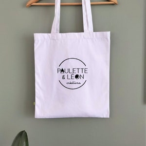 May include: White tote bag with black text and a logo that says "Paulette & Leon creations".