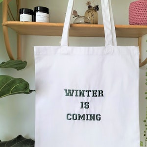 May include: White canvas tote bag with the text "Winter is Coming" embroidered in dark green.