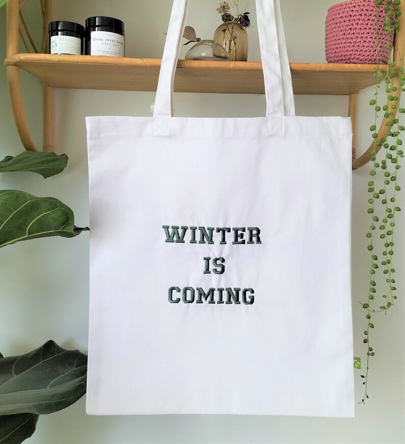 May include: White canvas tote bag with the text "Winter is Coming" embroidered in dark green.