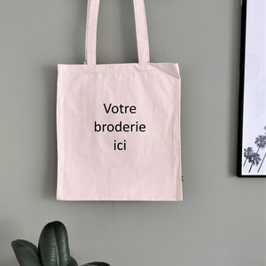 May include: A white tote bag with the text "Votre broderie ici" printed in black.