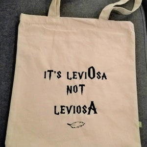 May include: A white canvas tote bag with black text that reads "It's LevioSA not LevioSA" and a small feather graphic.