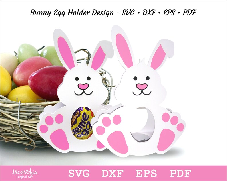 May include: Two white bunny shaped egg holders with pink ears and paws. The bunny's face has black eyes and a pink nose. The bunny's body has a cut-out to hold an egg. The bunny is sitting on a nest of straw.