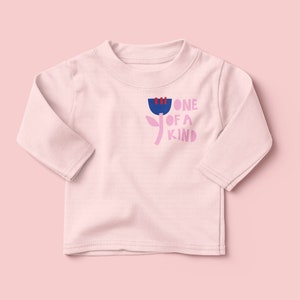 K&ouml;nnte beinhalten: Ein rosa Langarmshirt mit einem Blumenmotiv und dem Text "one of a kind" in Rosa, Blau und Rot.