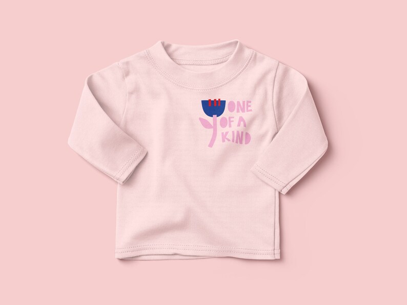 K&ouml;nnte beinhalten: Ein rosa Langarmshirt mit einem Blumenmotiv und dem Text "one of a kind" in Rosa, Blau und Rot.