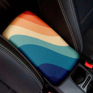 May include: A colorful car armrest cover with a wavy, abstract design in shades of blue, yellow, and orange.