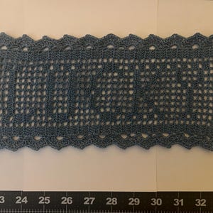 Puede incluir: Un tapete rectangular de ganchillo azul con un borde festoneado. La palabra "LOVE" está tejida en el centro del tapete. El tapete mide aproximadamente 30 cm de largo y 15 cm de ancho.