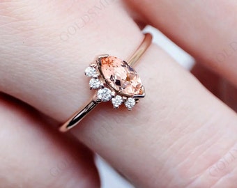 May include: A rose gold ring with a marquise-shaped peach morganite gemstone surrounded by a halo of smaller round diamonds.