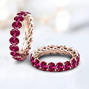 Peut inclure: Deux alliances éternelles avec un design délicat et complexe. Chaque alliance est sertie d'une rangée de pierres précieuses rubis de forme ovale.