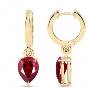 May include: Gold hoop earrings with a dangling pear-shaped ruby gemstone.