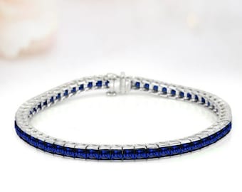 May include: A silver tennis bracelet with a row of blue sapphire stones.