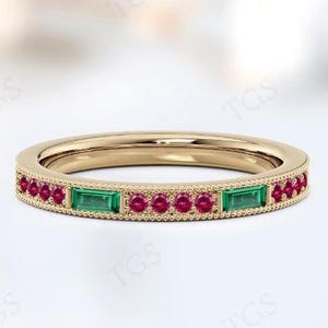 Op de afbeelding: Een gouden ring met een rij kleine rode edelstenen en twee grotere groene edelstenen.