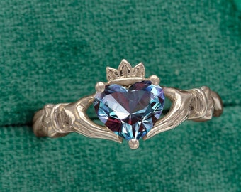 May include: A silver Claddagh ring with a blue heart-shaped gemstone. The ring features two hands clasping the heart, symbolizing love, friendship, and loyalty.