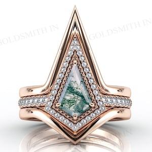 Puede incluir: Un anillo de compromiso de oro rosa con una piedra central de ágata verde musgo y un halo de diamantes. El anillo tiene un diseño puntiagudo y triangular y está engastado en una banda con diamantes más pequeños.