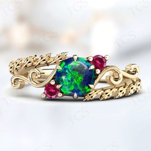 Op de afbeelding: Een gouden ring met een groene opaal-edelsteen en twee robijn accenten. De ring heeft een delicaat bladontwerp.