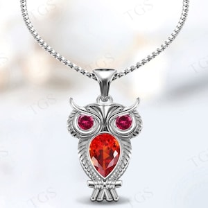 Puede incluir: Collar de plata con colgante de búho con piedras preciosas rojas y rosas. El búho tiene un diseño detallado y es un símbolo popular de sabiduría y conocimiento.