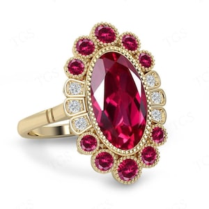 May include: A gold ring with a large oval ruby surrounded by smaller rubies and diamonds. The ring has a delicate, vintage-inspired design.