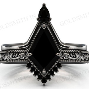 Könnte beinhalten: Verlobungsring mit schwarzem Diamanten, schwarzem Metallband und filigranen floralen Details. Der Ring hat einen großen, schwarzen, quadratischen Diamanten, der von kleineren schwarzen Diamanten umgeben ist.