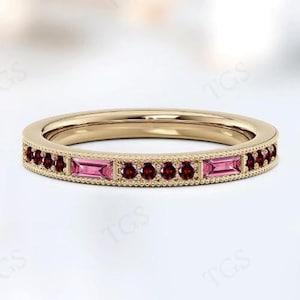 Puede incluir: Un anillo de banda de oro con una fila de piedras preciosas rosadas y rojas. El anillo tiene un diseño delicado de inspiración vintage.