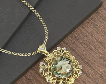 Può includere: Una collana con pendente dorato con una grande pietra preziosa ovale verde chiaro. Il pendente presenta un design a filigrana ornato con piccole pietre di accento trasparenti. La catena della collana è anch'essa dorata e il pendente è posto su uno sfondo scuro.