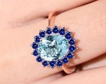 May include: A ring with a large, round, light blue gemstone surrounded by a halo of smaller, dark blue gemstones.