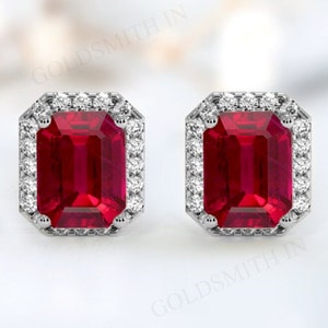May include: A pair of silver earrings with a red emerald-cut gemstone surrounded by a halo of smaller white gemstones.