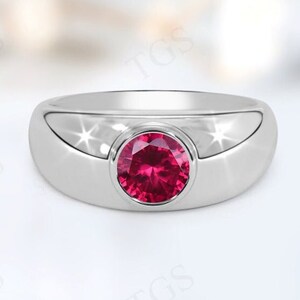 May include: A polished silver ring with a round, vibrant red gemstone set in the center. The ring has a smooth, curved design with a modern aesthetic. The gemstone is the focal point, catching the light and adding a pop of color.