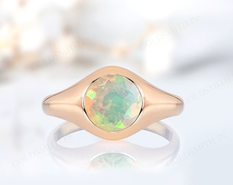 May include: A rose gold ring featuring a large, round opal gemstone. The opal displays a play of color with hues of green, yellow, and orange. The ring has a smooth, polished band and a bezel setting that securely holds the gemstone.