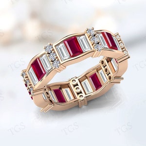 Puede incluir: Un anillo de banda de oro rosa con rubíes rojos y diamantes talla baguette transparentes alternados.