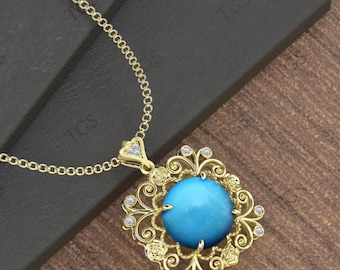 May include: A gold-colored necklace with a large, round, light blue gemstone pendant. The pendant is set in an ornate, square frame with small, clear accent stones. The necklace chain is also gold-colored.