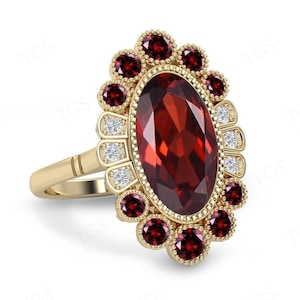 Puede incluir: Un anillo de oro con una gran piedra roja ovalada rodeada de piedras rojas más pequeñas y diamantes.