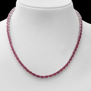 May include: A silver chain necklace with oval-shaped ruby red gemstones. The necklace is on a white mannequin bust.