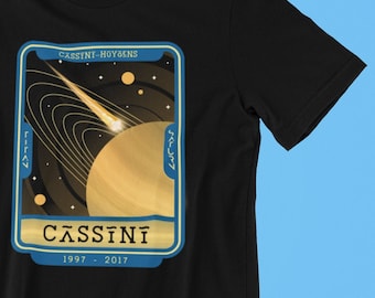 May include: Black t-shirt with a graphic of a planet with rings and a comet. The graphic is in a vintage style with a blue border and gold text that reads "CASSINI-HUYGENS" and "CASSINI 1997 - 2017".