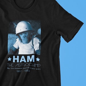 May include: Black t-shirt with a photo of a chimpanzee wearing a helmet. The text "HAM THE ASTROCHIMP" is printed on the shirt, along with the text "The first hominid launched into space 1957 - 1963".
