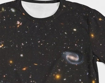Może przedstawiać: Czarny t-shirt z nadrukiem galaktyki, na ciemnym tle z rozproszonymi gwiazdami i galaktykami w różnych kolorach.