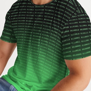 Op de afbeelding: Een zwart en groen T-shirt met korte mouwen met een verloop van binaire code. De code is groen en vervaagt naar zwart aan de bovenkant van het shirt.