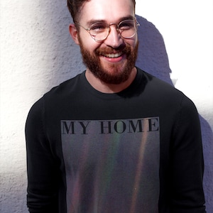 Puede incluir: Una camiseta negra de manga larga con un estampado gr&aacute;fico de una nebulosa colorida con el texto "MY HOME that pale BLUE DOT" en la parte delantera.