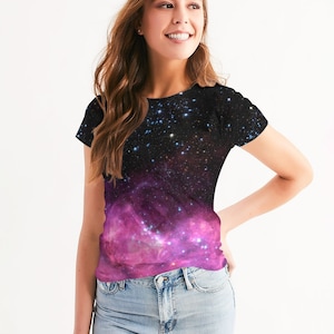 Puede incluir: Una mujer lleva una camiseta de manga corta con estampado de galaxia negro y rosa. La camiseta tiene un diseño de galaxia rosa descolorido en la parte inferior y un diseño de galaxia negro en la parte superior.