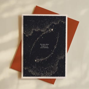 Könnte beinhalten: Geburtstagskarte mit dunkelblauem Hintergrund und Sternenmuster. Der Text lautet: "the stars shine brighter on your birthday". Die Karte liegt auf einem rostfarbenen Umschlag.