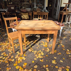 Könnte beinhalten: Ein hellfarbener Holztisch mit passendem Stuhl. Der Tisch hat eine rechteckige Platte und vier Beine. Der Stuhl hat eine Sprossenlehne. Die Szene spielt sich im Freien ab, mit gelben Herbstblättern auf dem Boden.