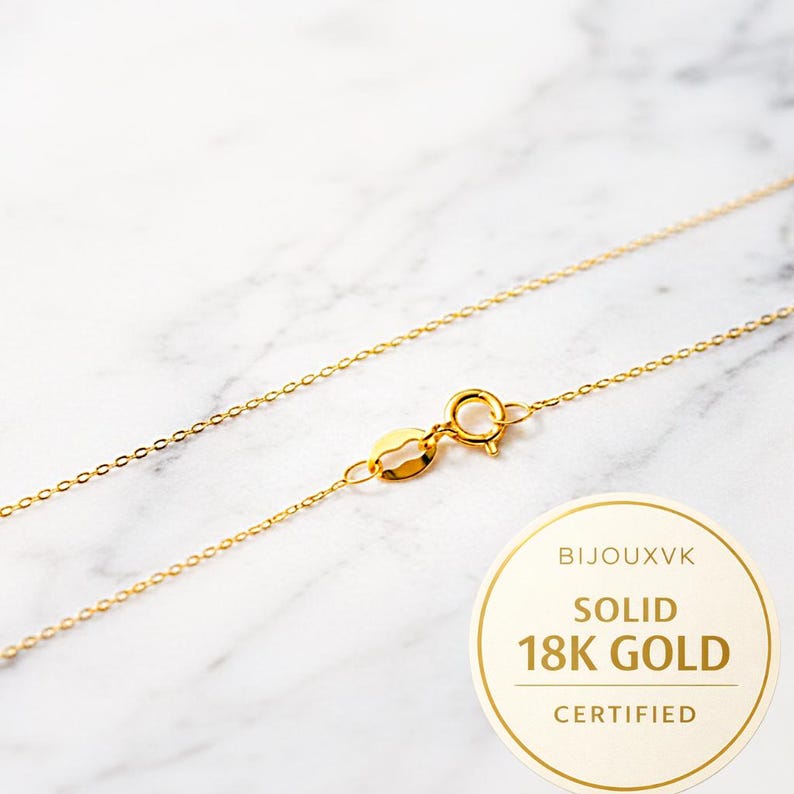 Puede incluir: Un delicado collar de oro con un cierre, sobre un fondo de m&aacute;rmol. El collar est&aacute; etiquetado como "SOLID 18K GOLD CERTIFIED" en una pegatina circular. La cadena est&aacute; hecha de peque&ntilde;os eslabones conectados.