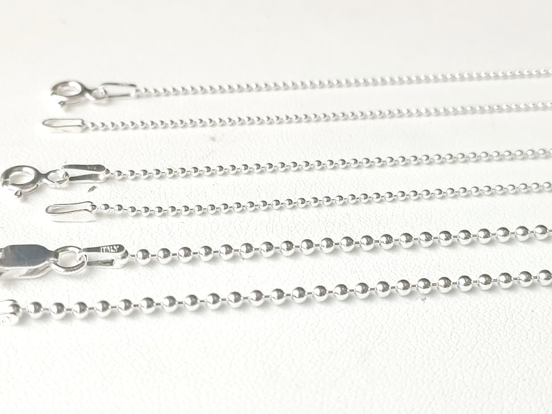 May include: Four silver ball chain necklaces of varying lengths, displayed on a white surface.
