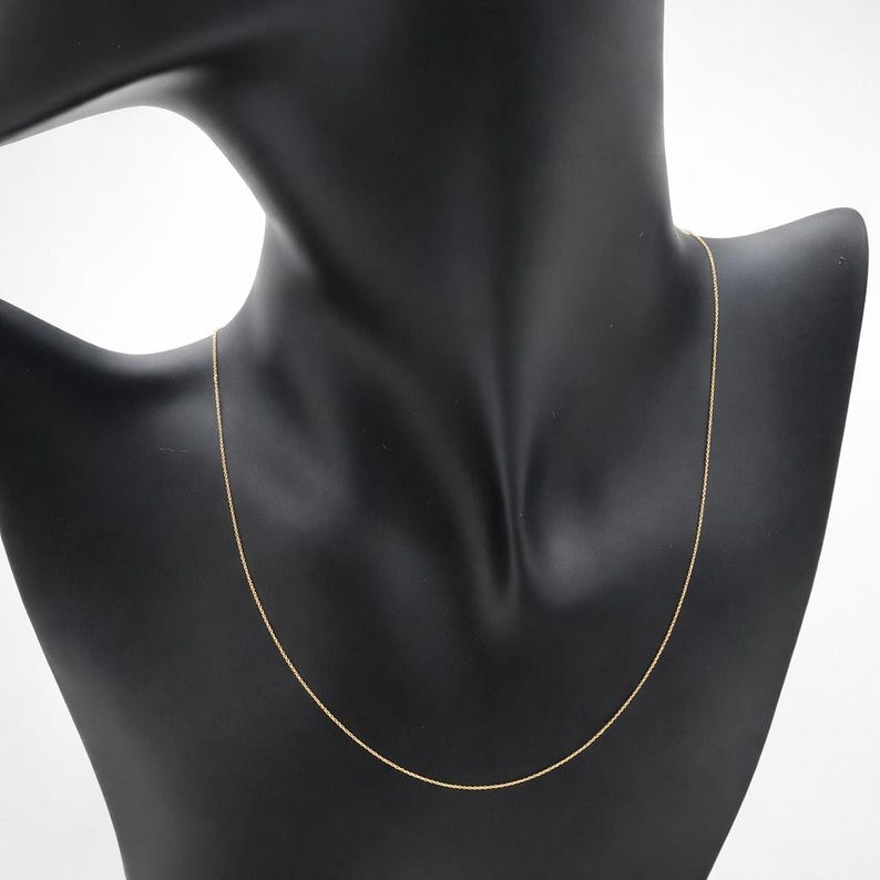 Puede incluir: Un delicado collar de cadena de color dorado exhibido en un maniqu&iacute; negro. El collar es delgado y parece estar hecho de peque&ntilde;os eslabones conectados. La cadena est&aacute; drapeada alrededor del cuello del maniqu&iacute;, mostrando su longitud y dise&ntilde;o.