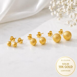 May include: Three pairs of gold stud earrings featuring spherical beads with a textured matte finish. Each earring has a post back. A circular white label in the corner displays the text BIJOUXVK SOLID 18K GOLD CERTIFIED in gold lettering.