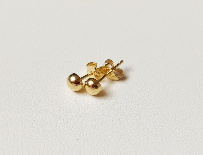 Pu&ograve; includere: Un paio di orecchini a bottone in oro con un design rotondo.