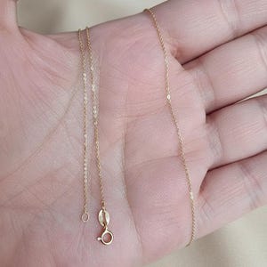 Puede incluir: Un delicado collar de cadena de color dorado con un peque&ntilde;o cierre y un anillo circular. El collar se muestra sobre una superficie de color claro. La cadena es fina y parece estar hecha de peque&ntilde;os eslabones conectados.