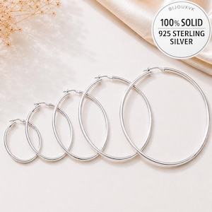 Puede incluir: Un conjunto de cuatro pendientes de aro de plata en tamaños graduados, dispuestos de menor a mayor. Cada pendiente presenta una banda circular fina con cierre de poste articulado. Una etiqueta circular indica BIJOUXVK 100% SOLID 925 STERLING SILVER.