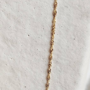 May include: A gold chain necklace with a delicate, twisted design. The chain is on a white background.
